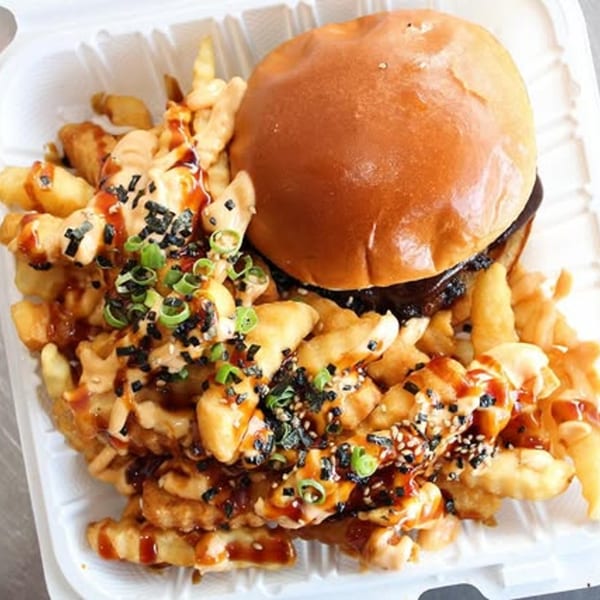 A Wailua Drive In burger and waffle fries topped with sauces, sesame seeds, and green onions.