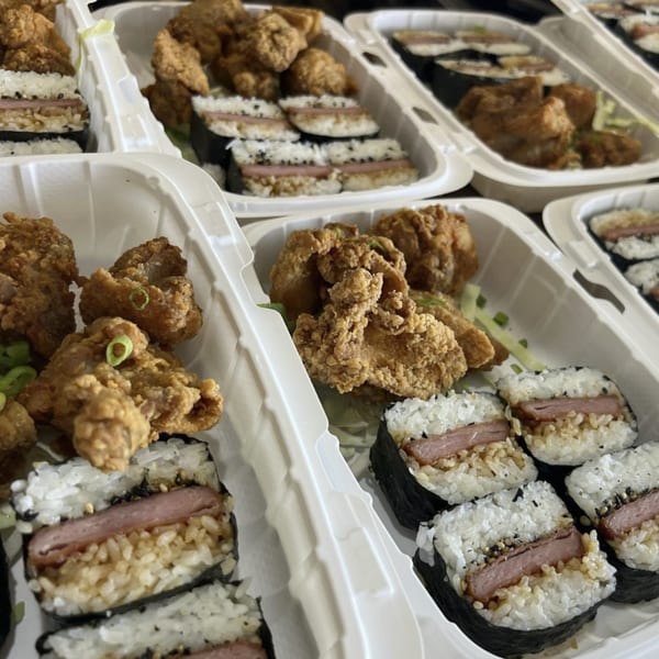 Multiple takeout containers filled with Hawaiian fried chicken and Spam musubi with rice and nori.